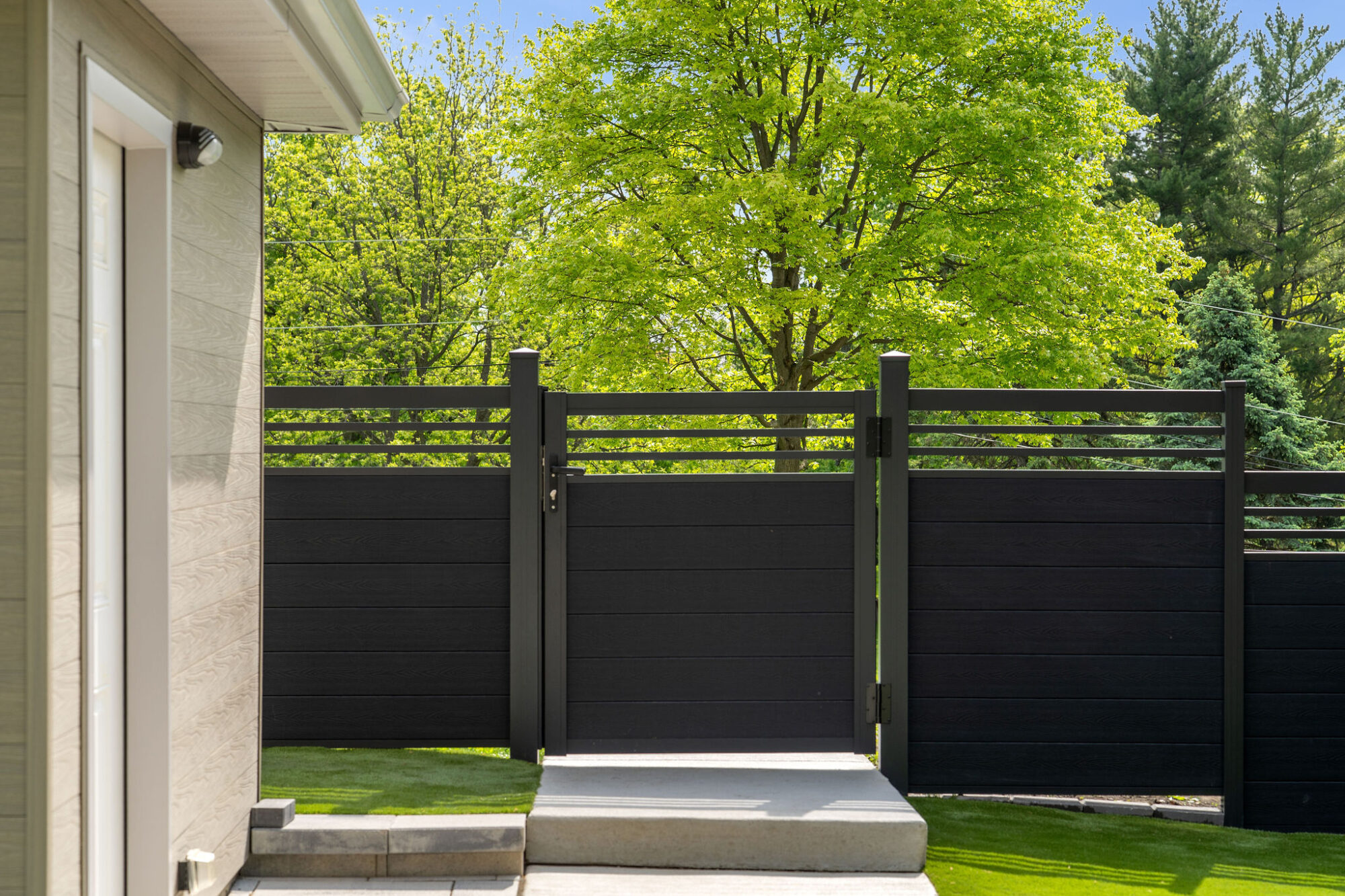 GWF® Classic Trellis Charcoal Composite Gate Entry GWF® Classic Trellis charcoal composite pool gate set between fence runs at the end of a concrete path, open crown trellis matching the adjacent panels