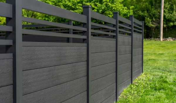 GWF® Classic Trellis charcoal composite fence along a manicured lawn, slim matte black aluminum trellis rails forming an open crown above solid woodgrain panels