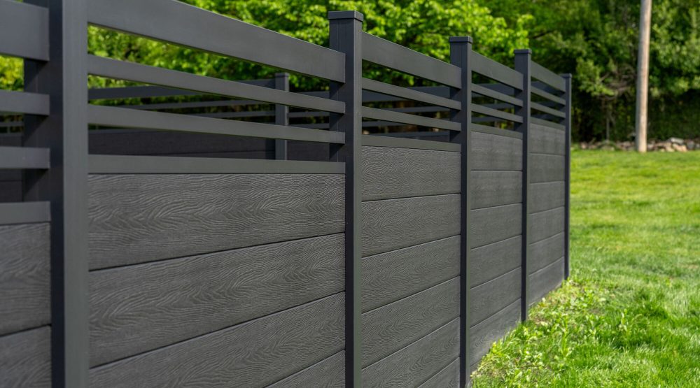 GWF® Classic Trellis charcoal composite fence along a manicured lawn, slim matte black aluminum trellis rails forming an open crown above solid woodgrain panels