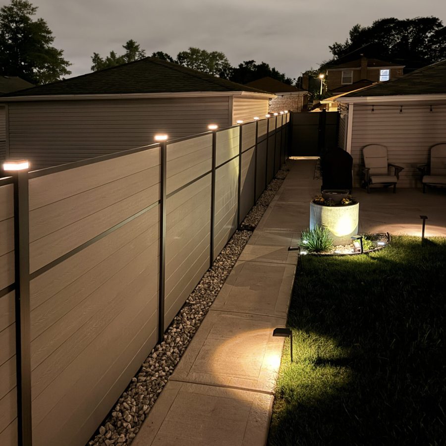 Greenwood Fence Classic Privacy fence in Storm Grey composite at night with illuminated GWF solar LED post caps along a lit garden path